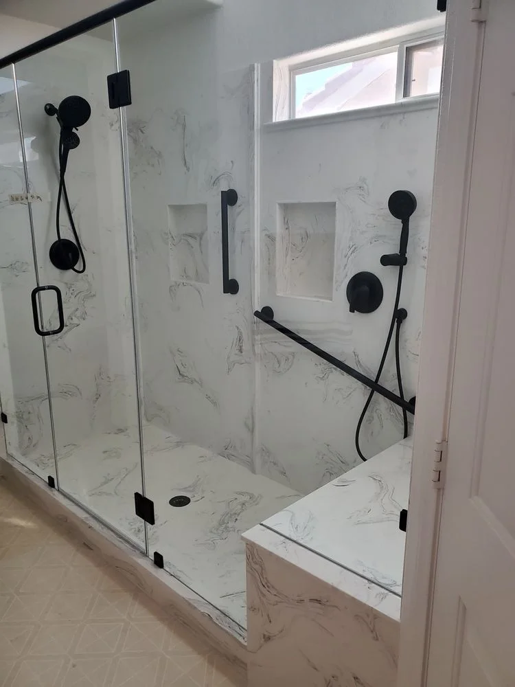 Marble-patterned walk-in shower with black fixtures, grab bars, and a built-in bench