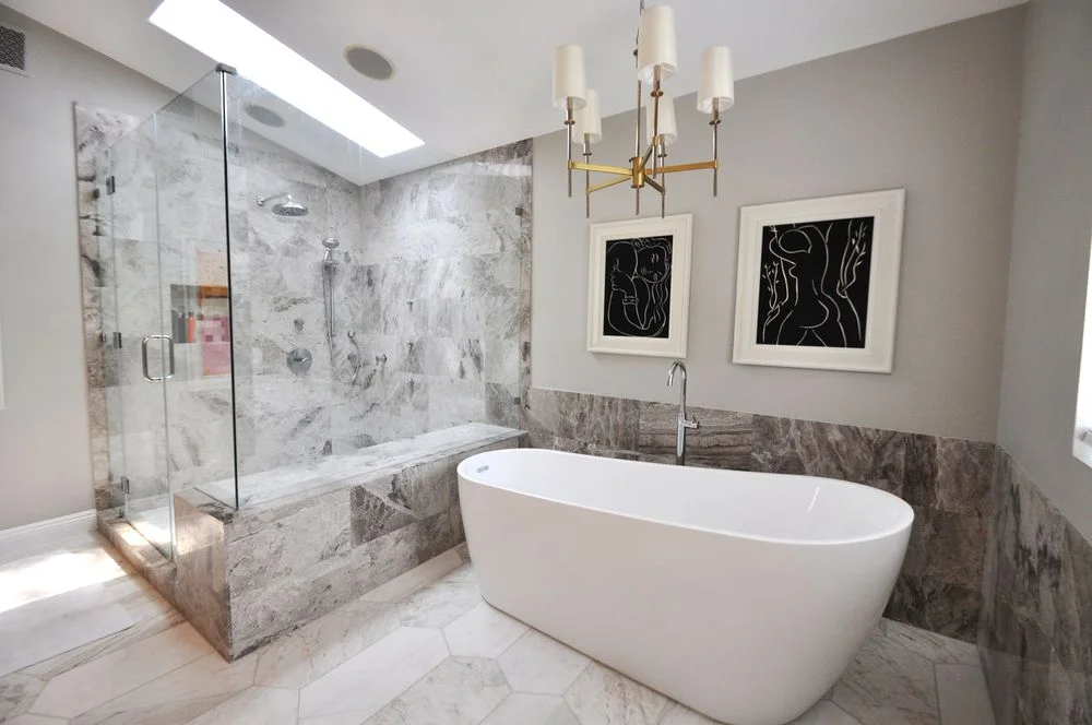 White freestanding bathtub beside a glass-enclosed marble-patterned shower